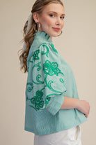 Woman wearing a light blue blouse with green floral patterns on a beige background
