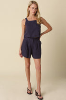 Woman wearing a navy sleeveless top and shorts on a beige background