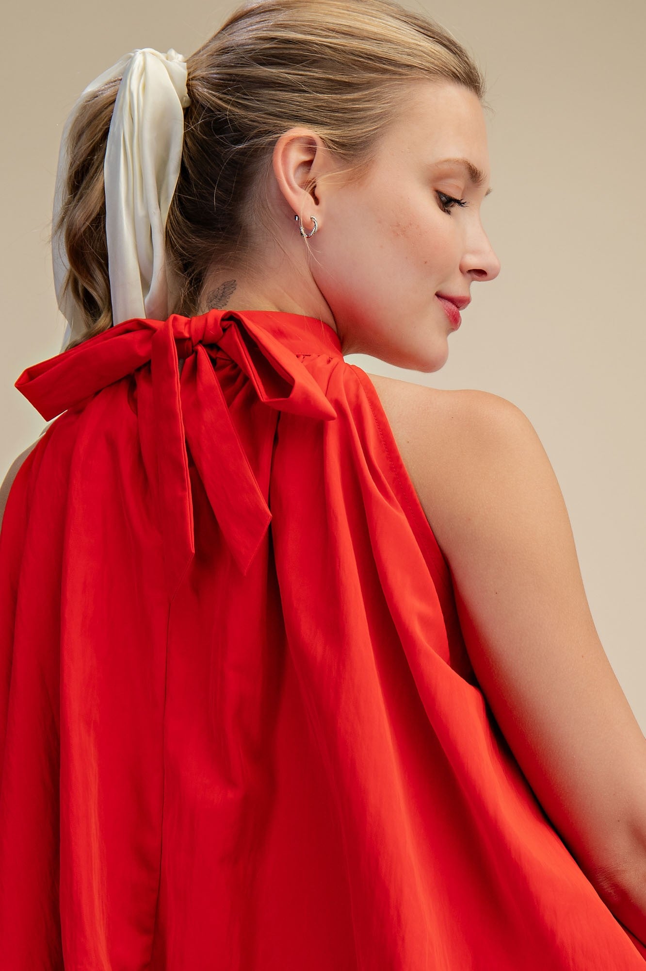 Woman wearing a red dress with a bow detail on a beige background
