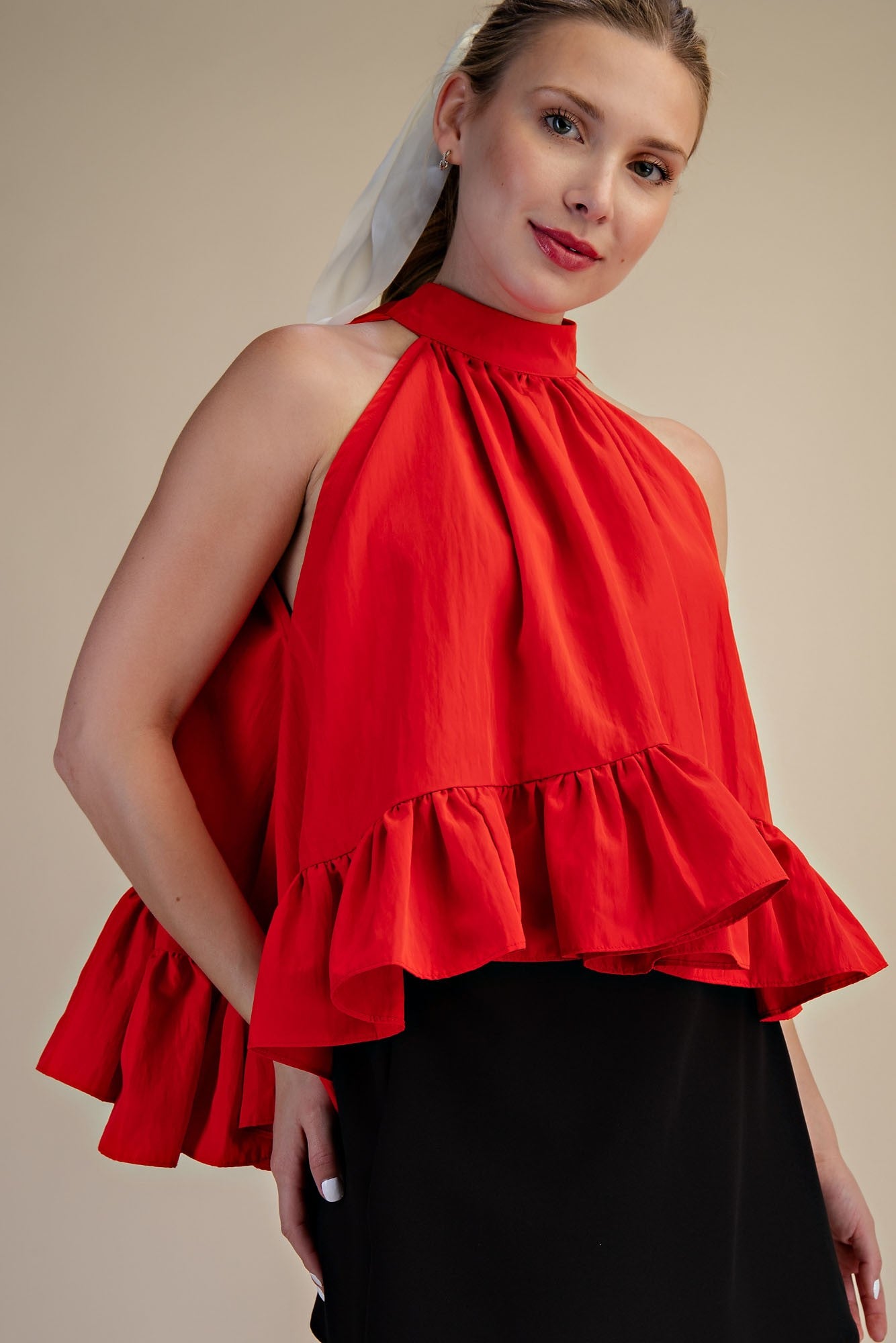 Woman wearing a red halter top with ruffles on a beige background