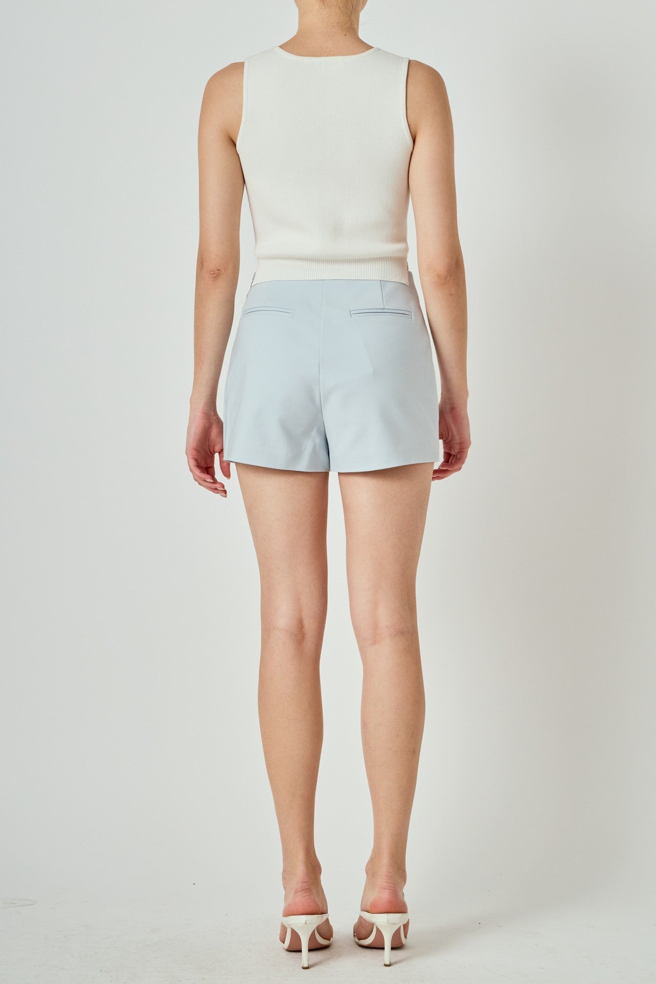Person wearing a white sleeveless top and light blue shorts on a plain background