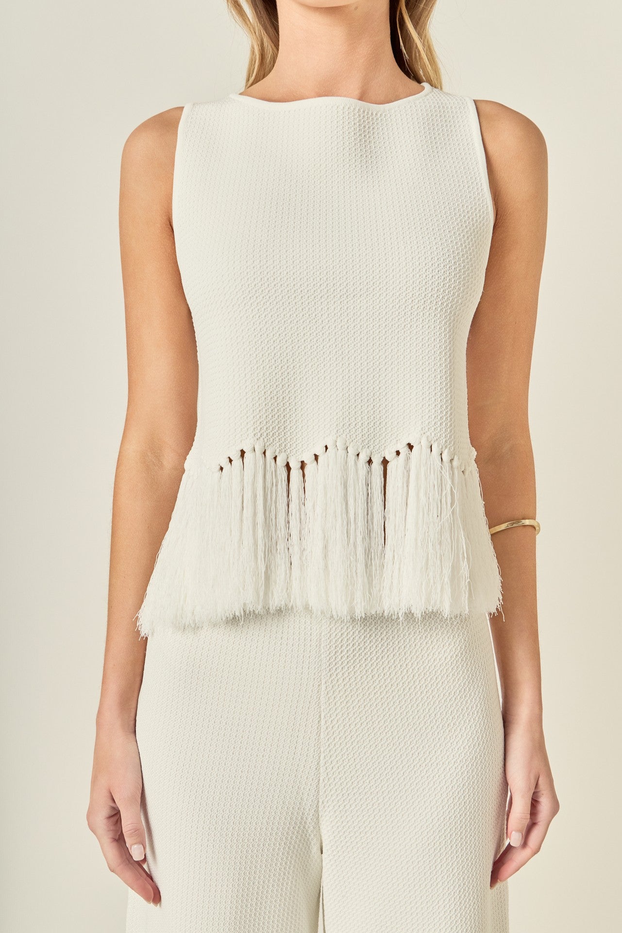 White sleeveless top with fringe details on a neutral background
