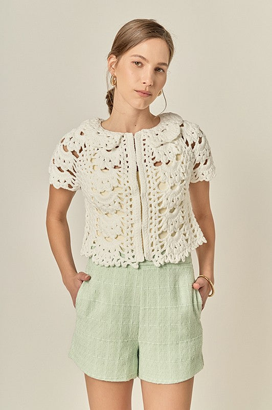 Woman wearing a white lace top and light green shorts on a beige background