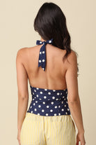 Woman wearing a navy blue halter top with white polka dots and yellow pants on a beige background