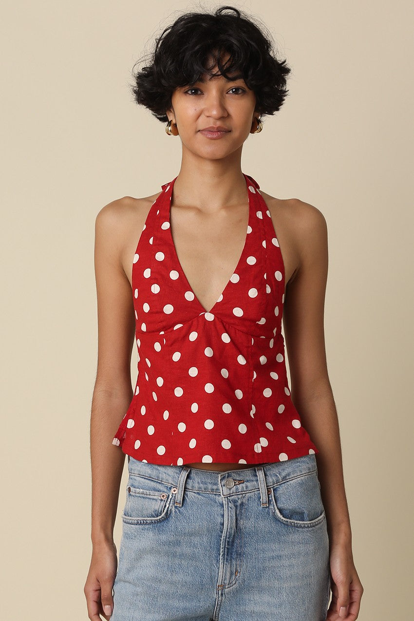 Woman wearing a red polka dot halter top and blue jeans against a beige background