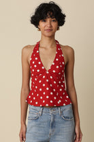 Woman wearing a red polka dot halter top and blue jeans against a beige background