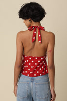 Person wearing a red polka dot top with a halter neck and tied back, standing against a beige background.