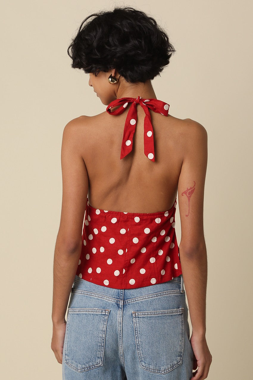 Person wearing a red polka dot top with a halter neck and tied back, standing against a beige background.