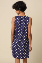 Woman wearing a navy dress with white polka dots against a beige background