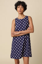 Woman wearing a navy dress with white polka dots against a beige background