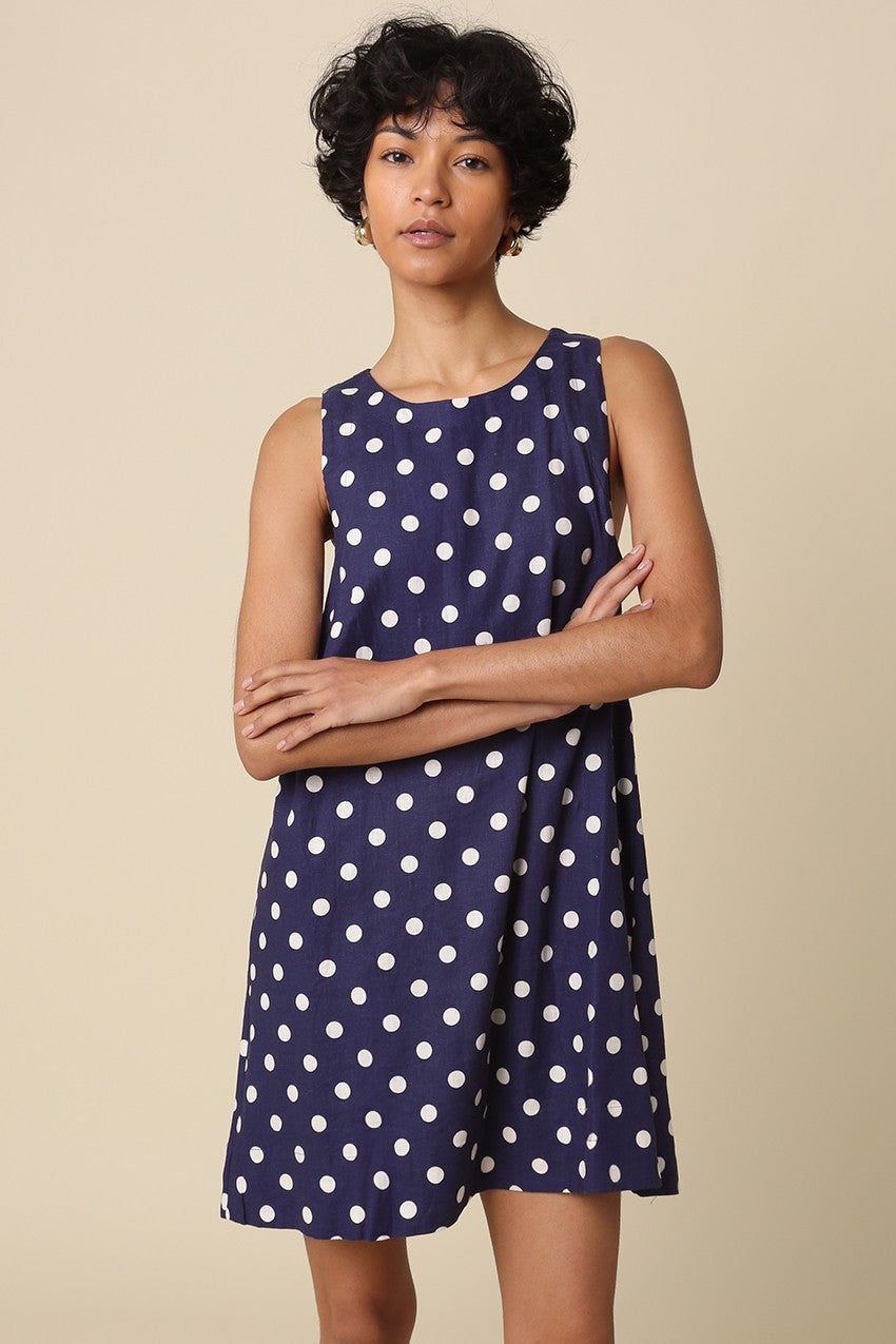 Woman wearing a navy dress with white polka dots against a beige background