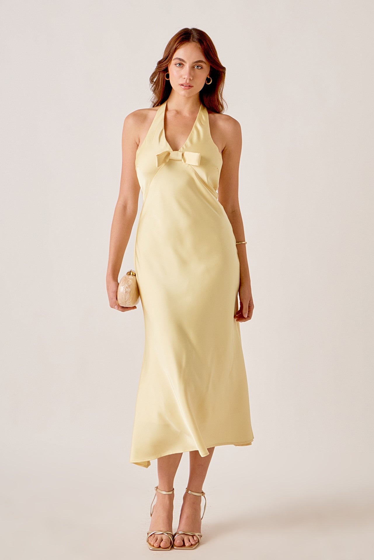Woman wearing a yellow dress with a bow detail on a plain background