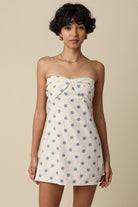 Woman wearing a strapless dress with blue polka dots on a beige background