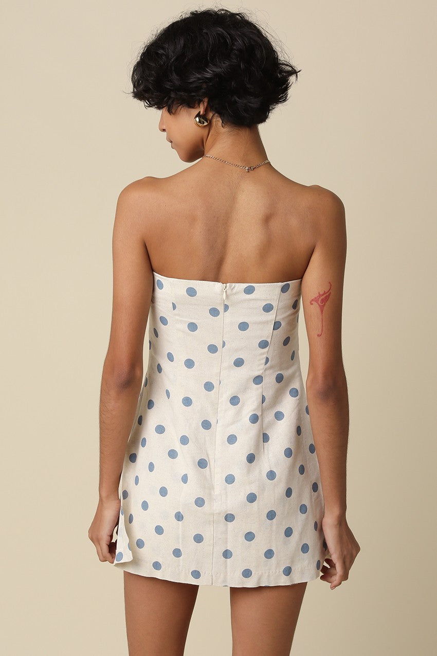 Woman wearing a strapless polka dot dress against a beige background