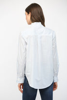 Woman wearing a white shirt with blue stripes and dark jeans on a white background
