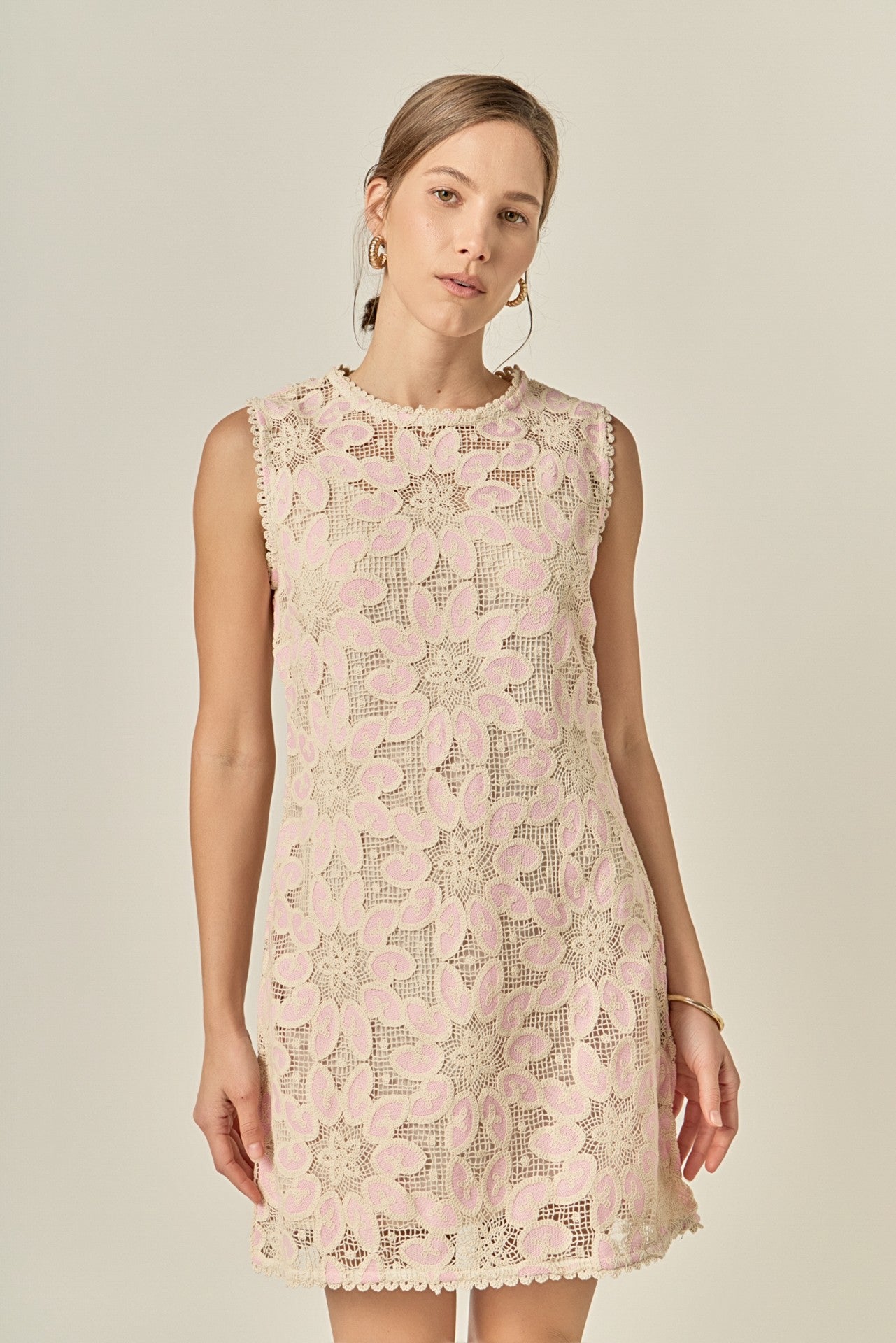 Woman wearing a light pink lace dress with a subtle pattern on a beige background