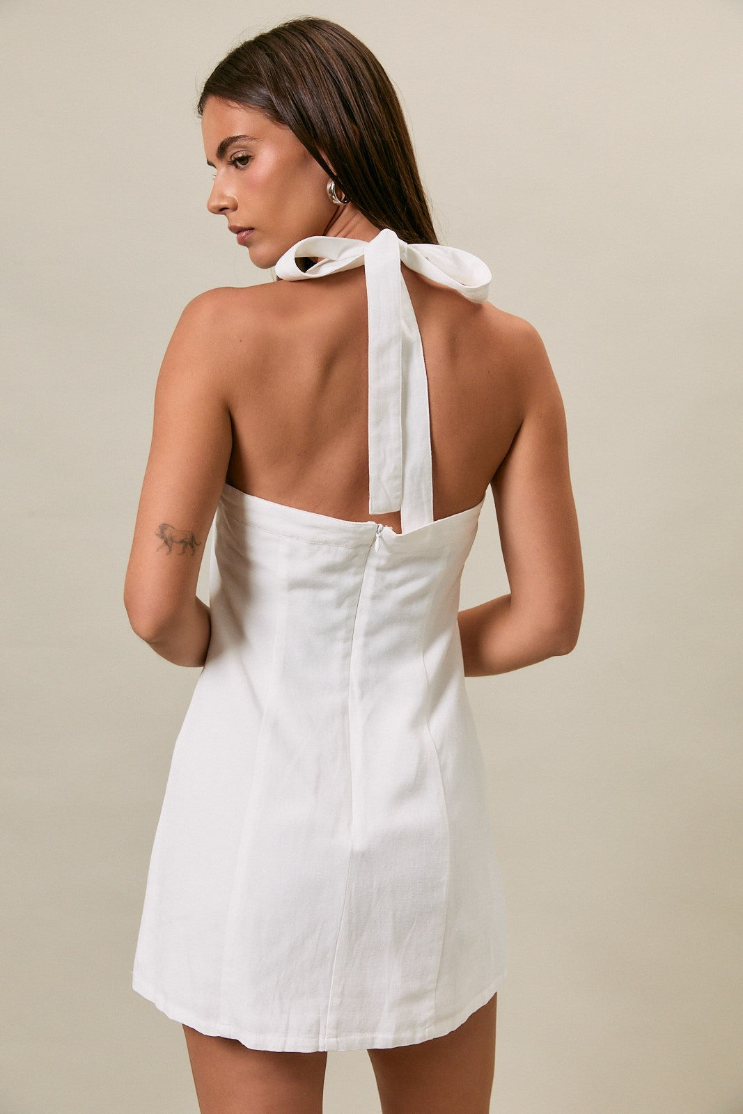 Woman wearing a white dress with a bow detail on a beige background