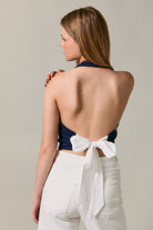 Woman wearing a blue top with a white bow and white pants on a neutral background