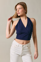 Woman wearing a navy halter top and white pants against a neutral background