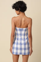Woman wearing a blue and white checkered strapless dress on a beige background