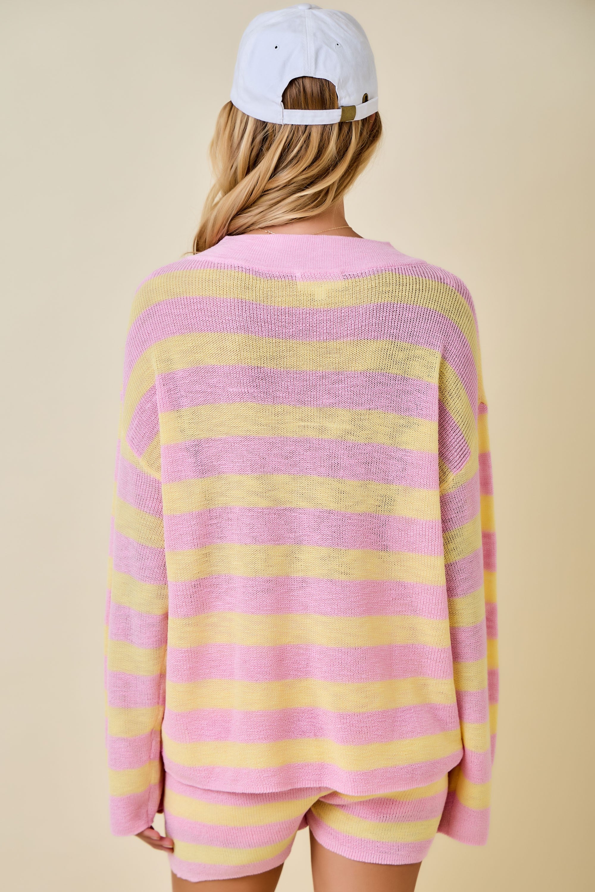Person wearing a pink and yellow striped sweater with a beige background