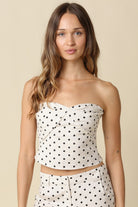 Woman wearing a polka dot strapless top and pants on a beige background