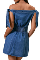 Woman wearing a blue denim dress with bow straps on a beige background