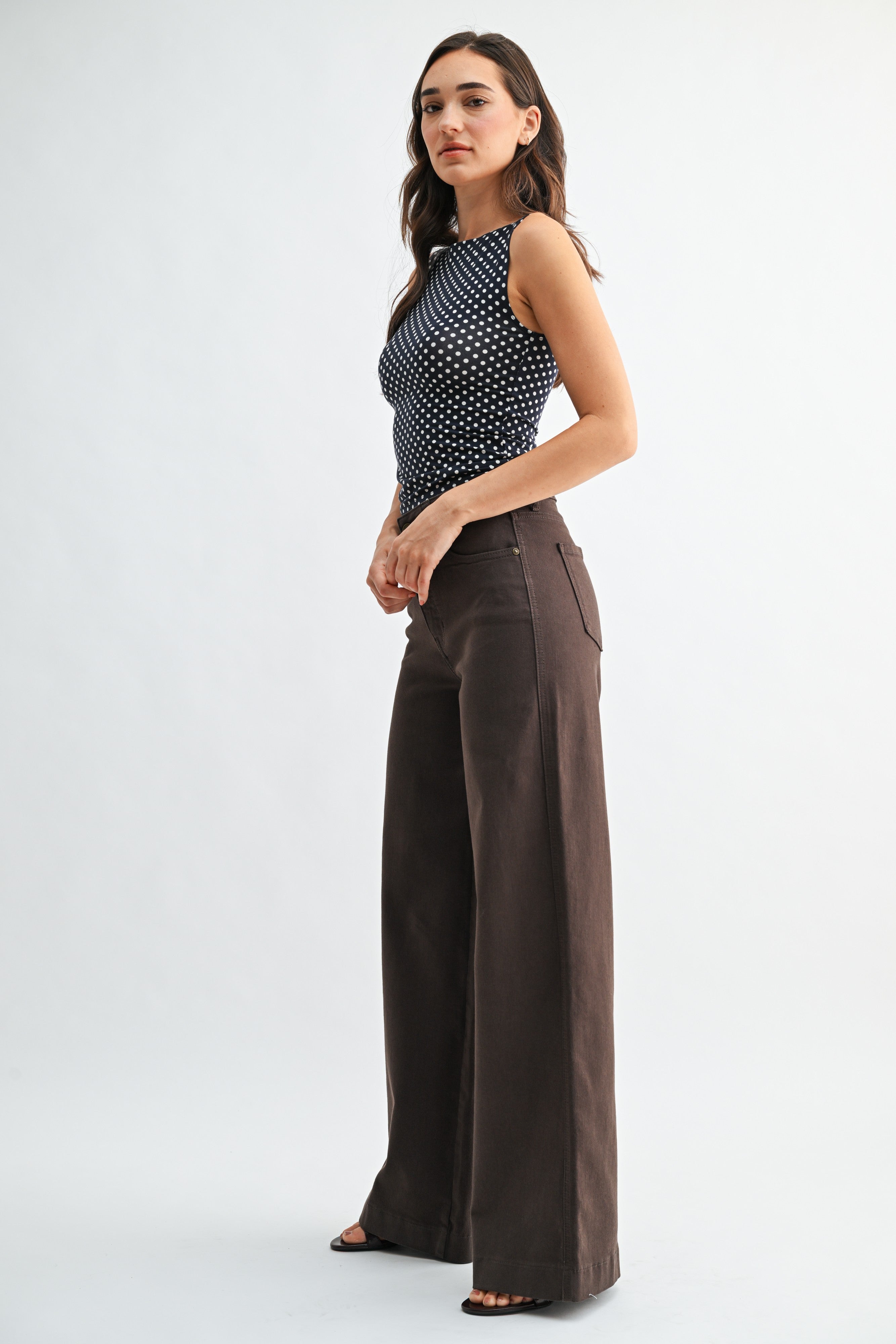 Woman wearing a black and white polka dot top and brown wide-leg pants on a white background