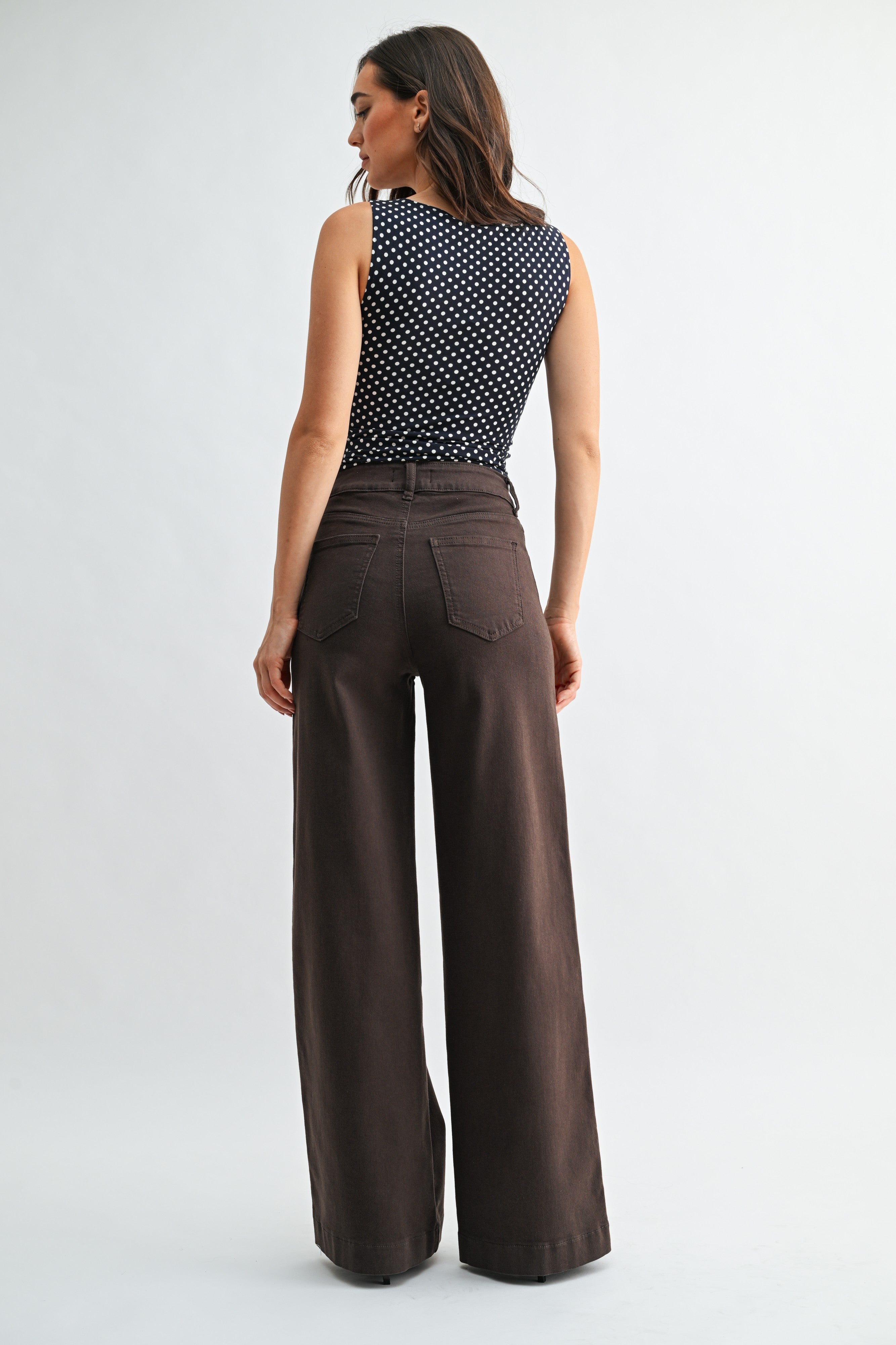 Woman wearing a polka dot top and brown wide-leg pants on a white background