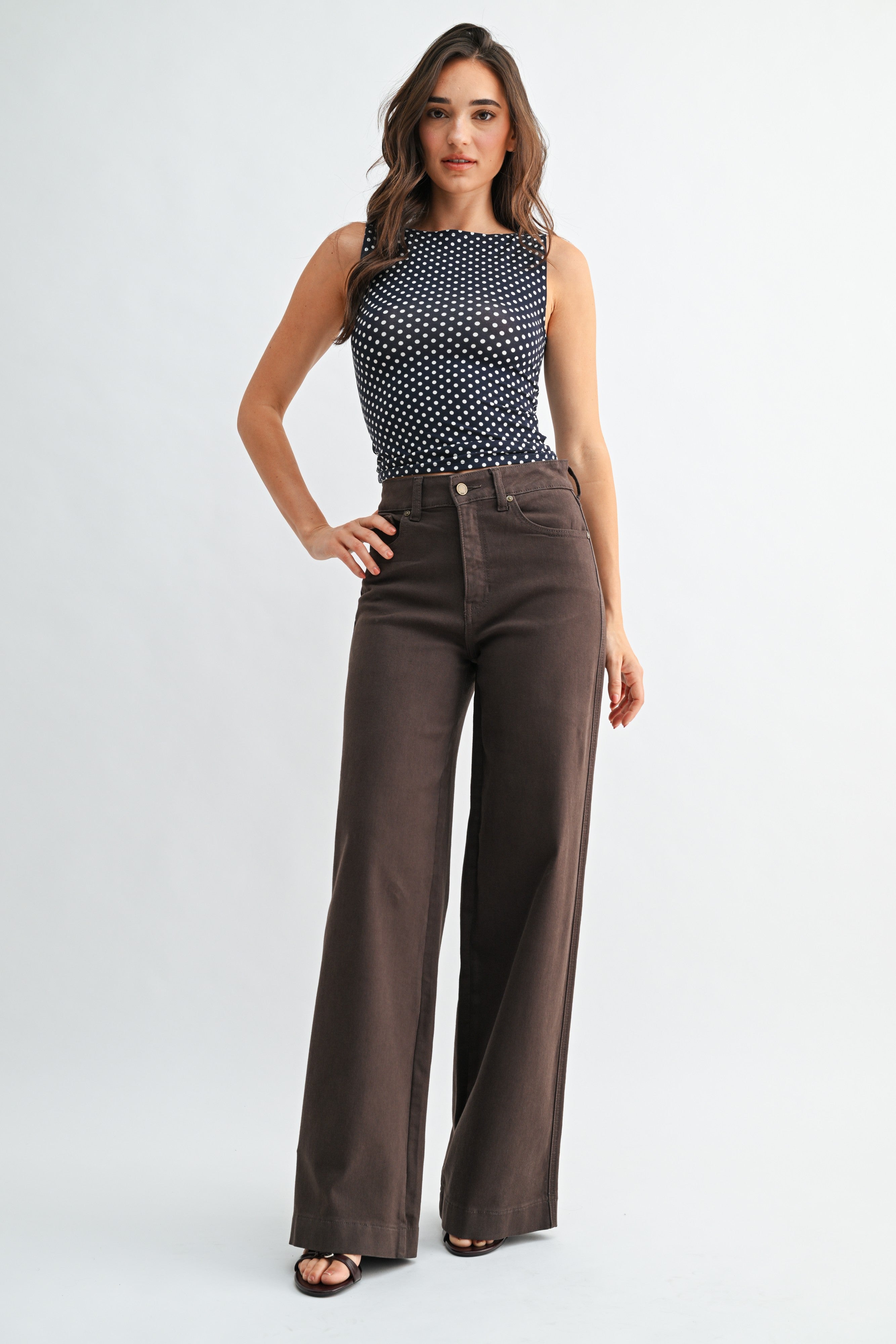 Woman wearing a sleeveless patterned top and brown flared pants on a white background