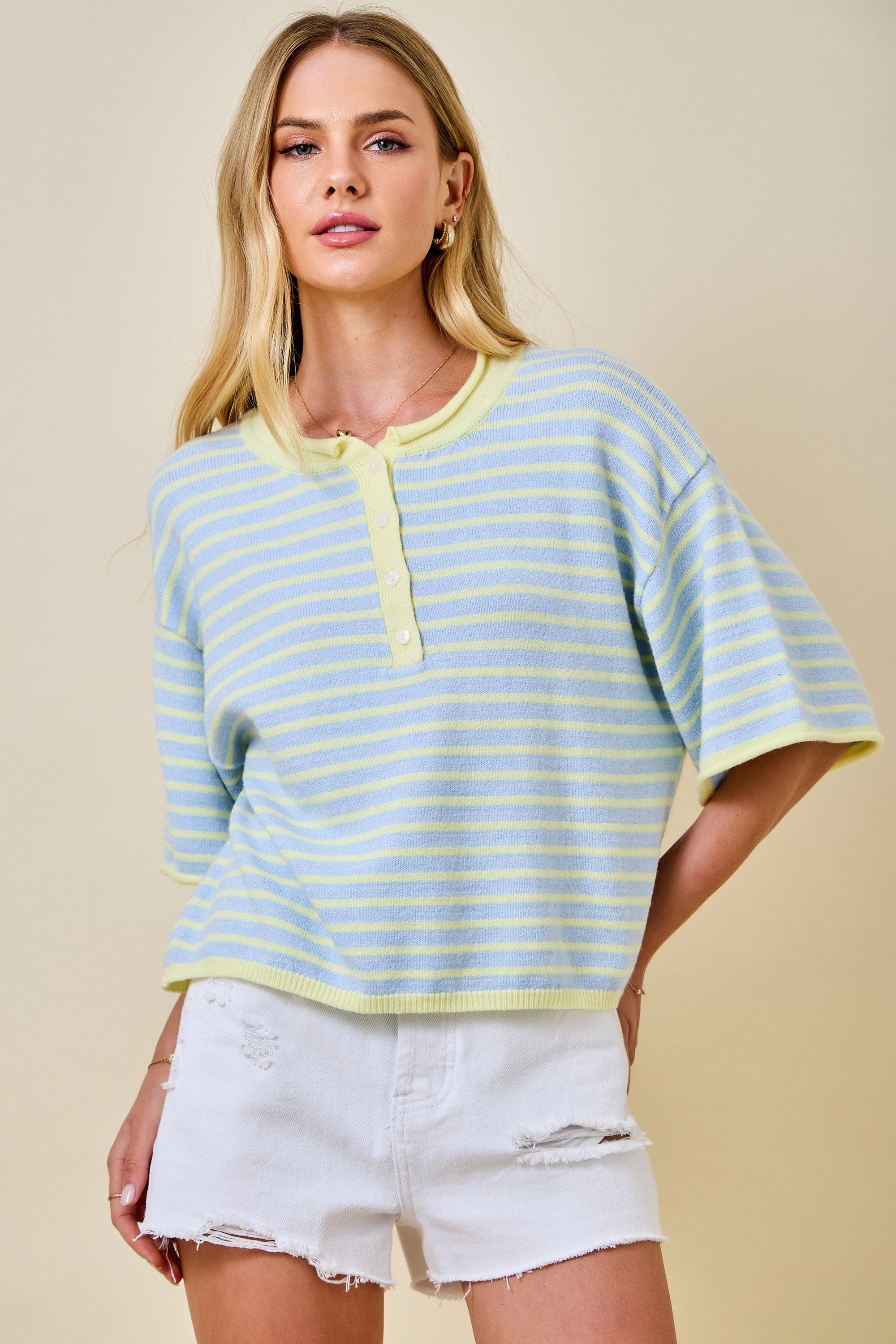 Woman wearing a light blue and yellow striped top with white shorts on a beige background
