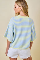 Woman wearing a light blue and yellow striped sweater with white shorts on a beige background