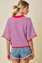 Woman wearing a red and white striped shirt with denim shorts on a beige background