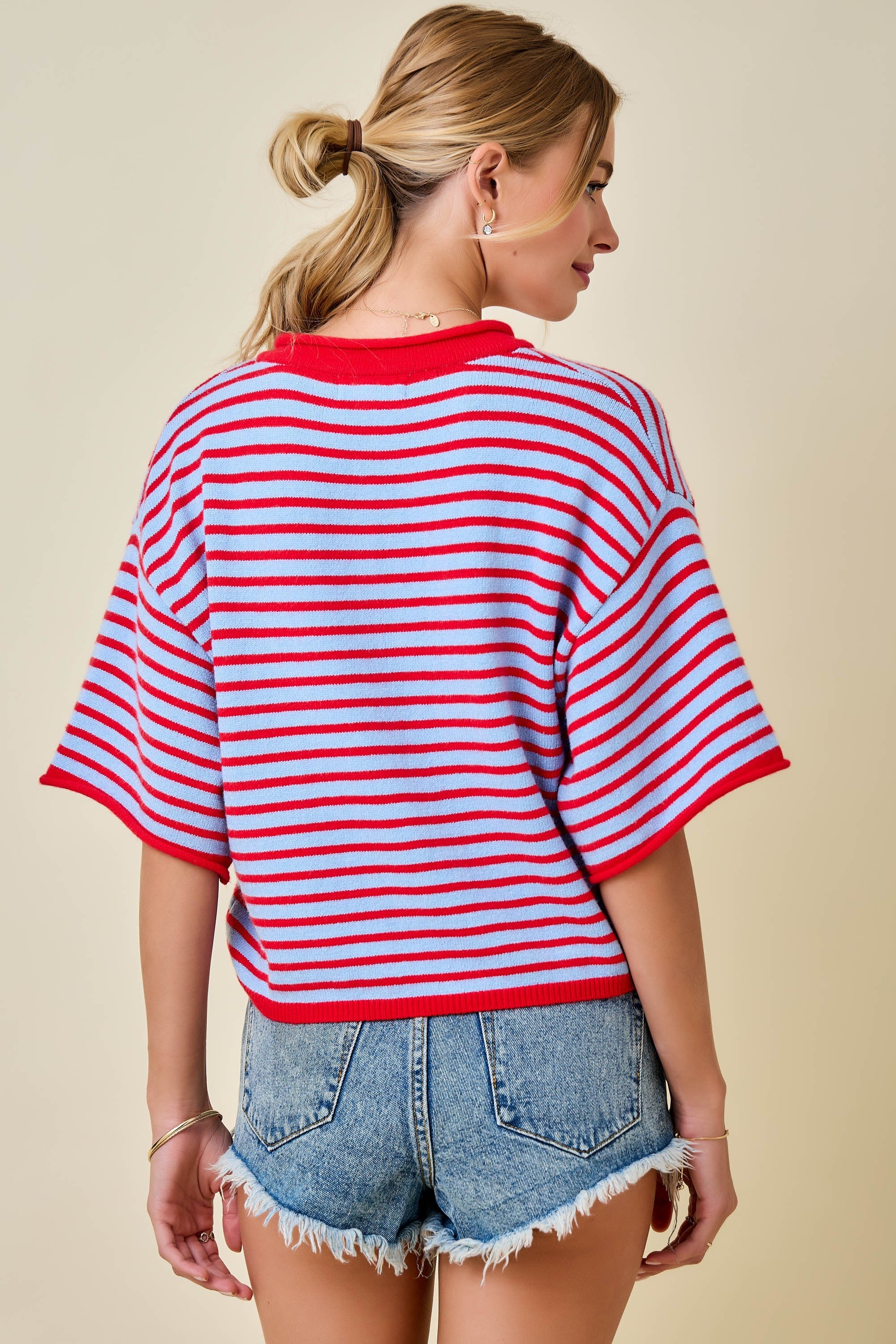 Woman wearing a red and white striped shirt with denim shorts on a beige background