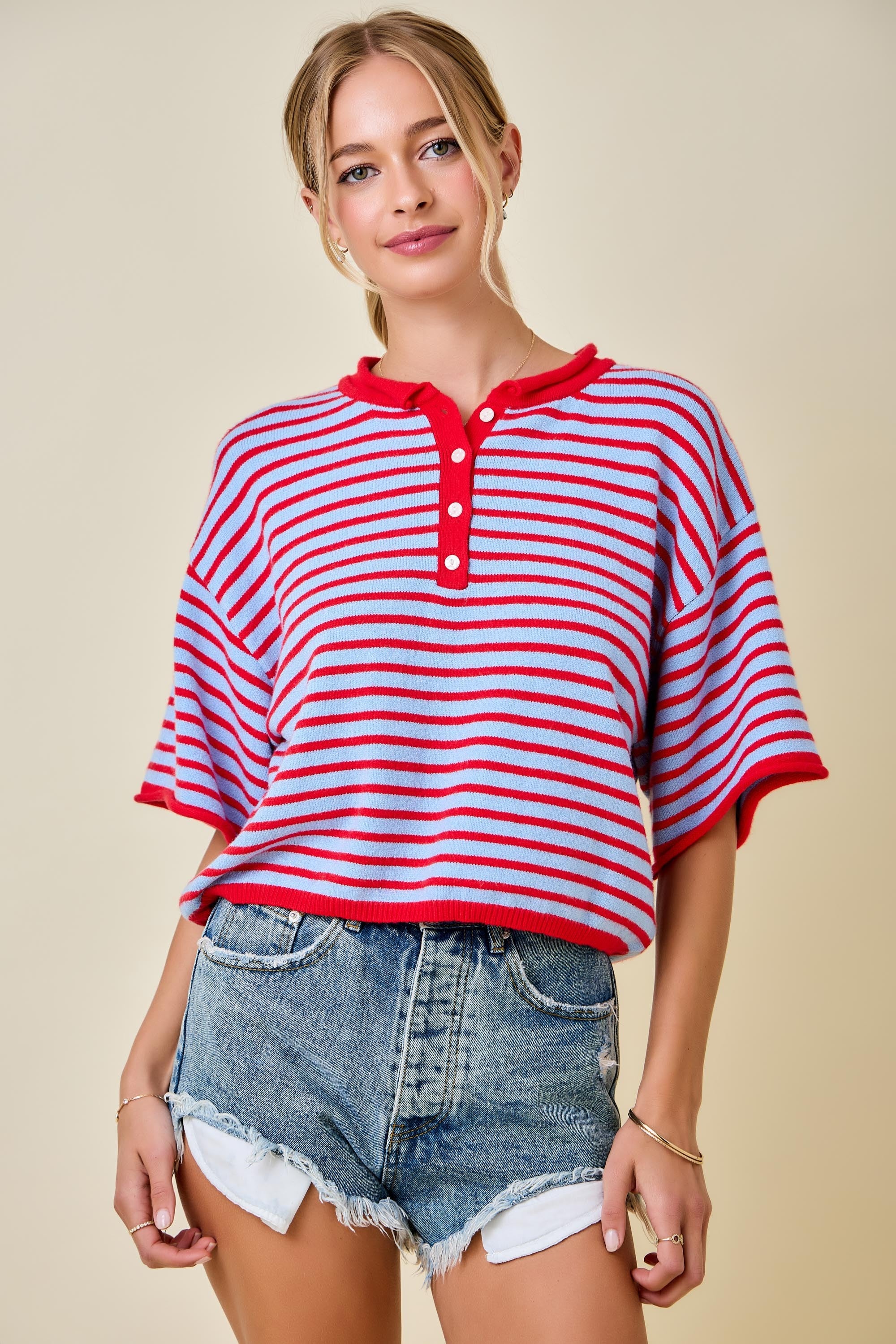 Woman wearing a red and white striped shirt with denim shorts on a beige background