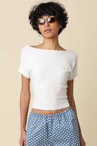 Woman wearing a white top and blue polka dot pants against a beige background