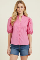 Woman wearing a pink blouse with puff sleeves and denim shorts on a beige background