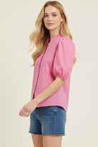 Woman wearing a pink blouse with puff sleeves and denim shorts on a beige background