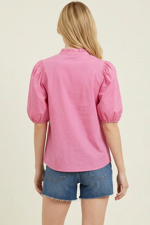 Person wearing a pink blouse with puff sleeves and denim shorts on a beige background
