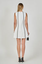 Woman wearing a white sleeveless dress with black trim on a plain background