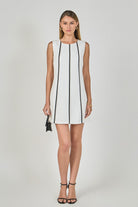 Woman wearing a white dress with black trim on a plain background