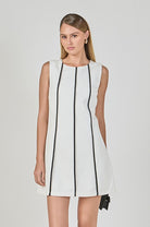 Woman wearing a white dress with black accents on a plain background