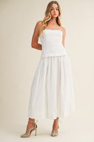 Woman wearing a strapless white dress against a plain background