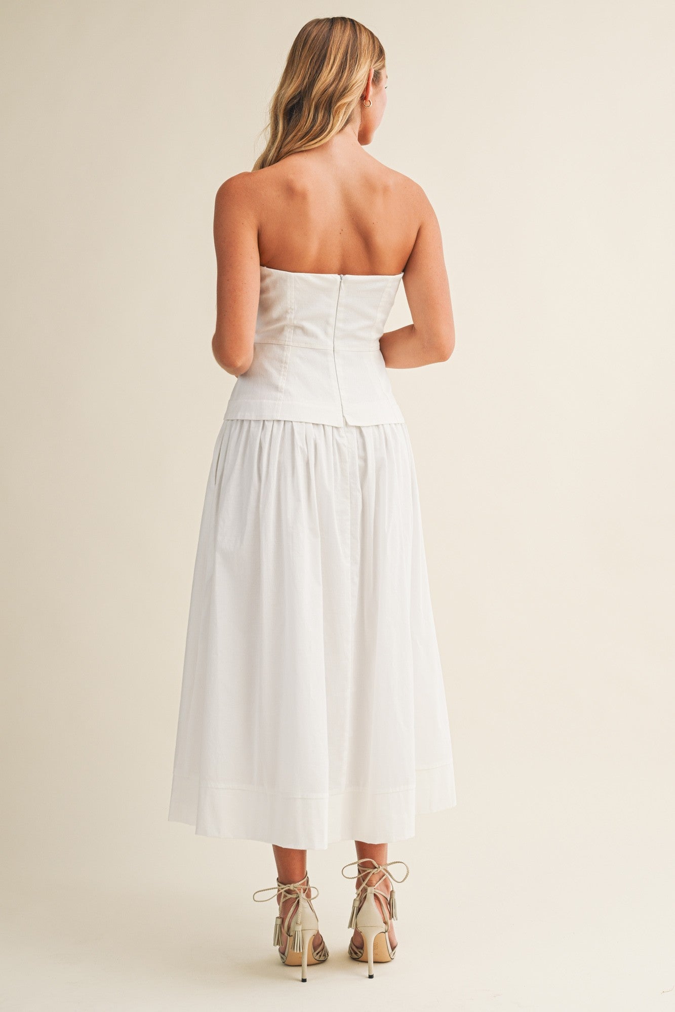 Woman wearing a strapless white dress against a plain background