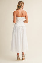 Woman wearing a strapless white dress against a plain background