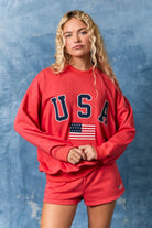 Person wearing a red 'USA' sweatshirt with an American flag against a blue textured background