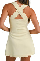 Woman wearing a light yellow dress with a scalloped hem and open back on a plain background