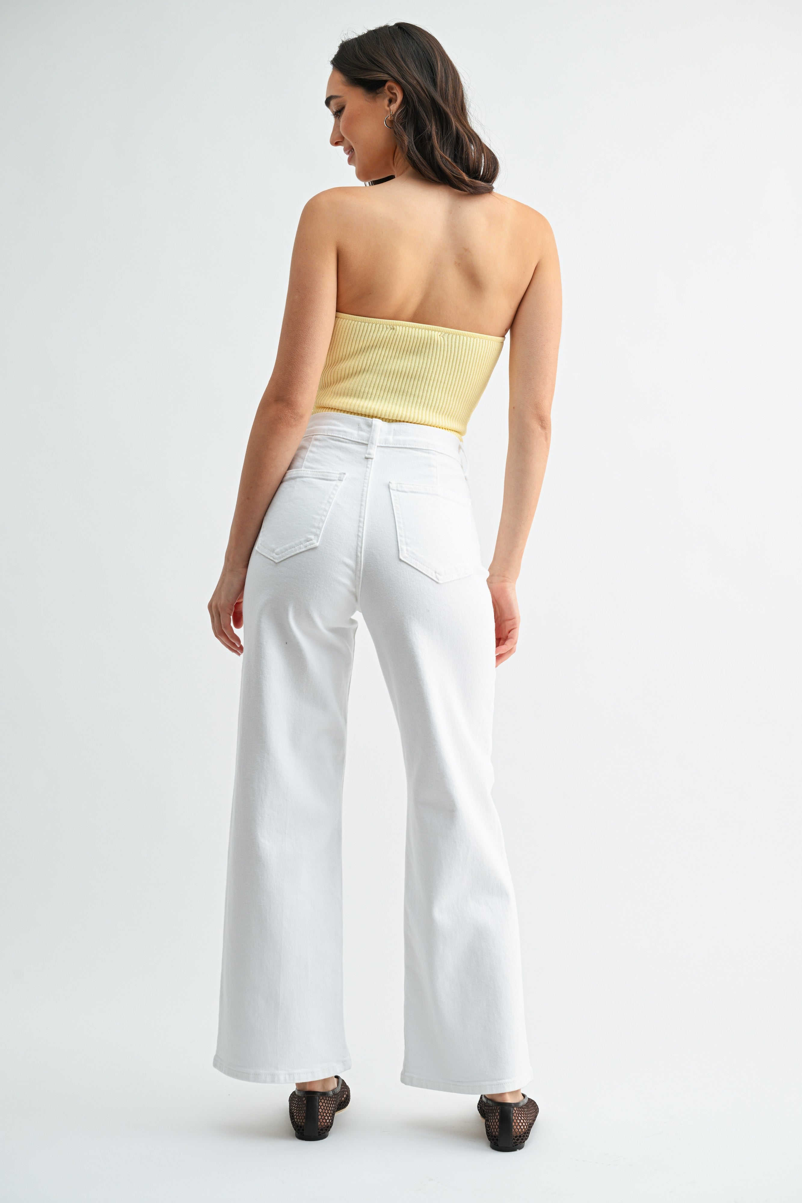 Woman wearing a strapless yellow top and white pants on a light gray background