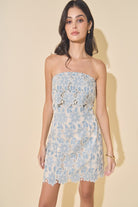 Woman wearing a blue floral lace dress against a beige background