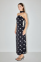 A woman modeling a strapless black maxi dress with large white polka dots and a matching black halter-style neck band, standing against a plain light gray studio background.